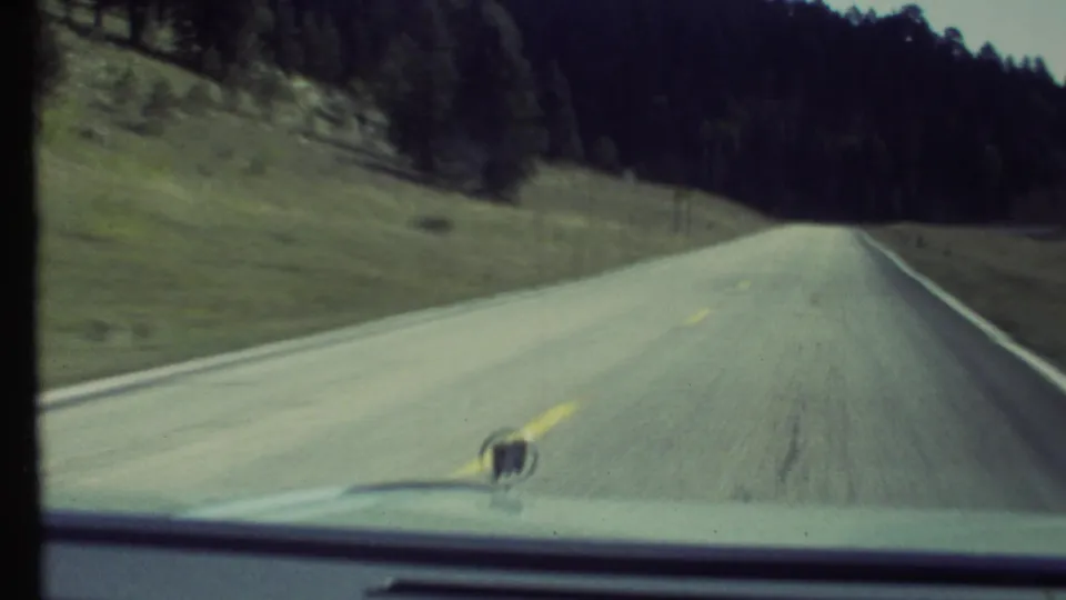 1972 home-movie frame from a moving car on a two-lane road through a grassy, wooded landscape in the Grand Canyon, Arizona area.