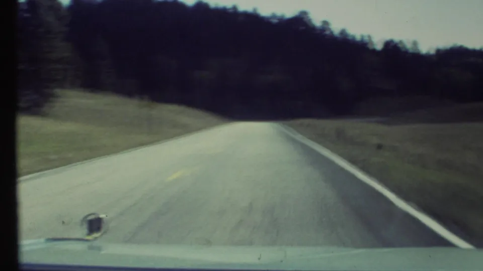 End frame of a 1972 8mm car POV near Grand Canyon, Arizona, showing a road leading toward darker trees and hills.