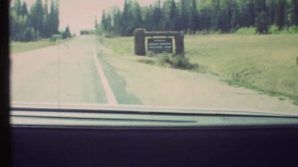 1972 8mm view from a car nearing the Grand Canyon National Park entrance sign on a wooded roadside.