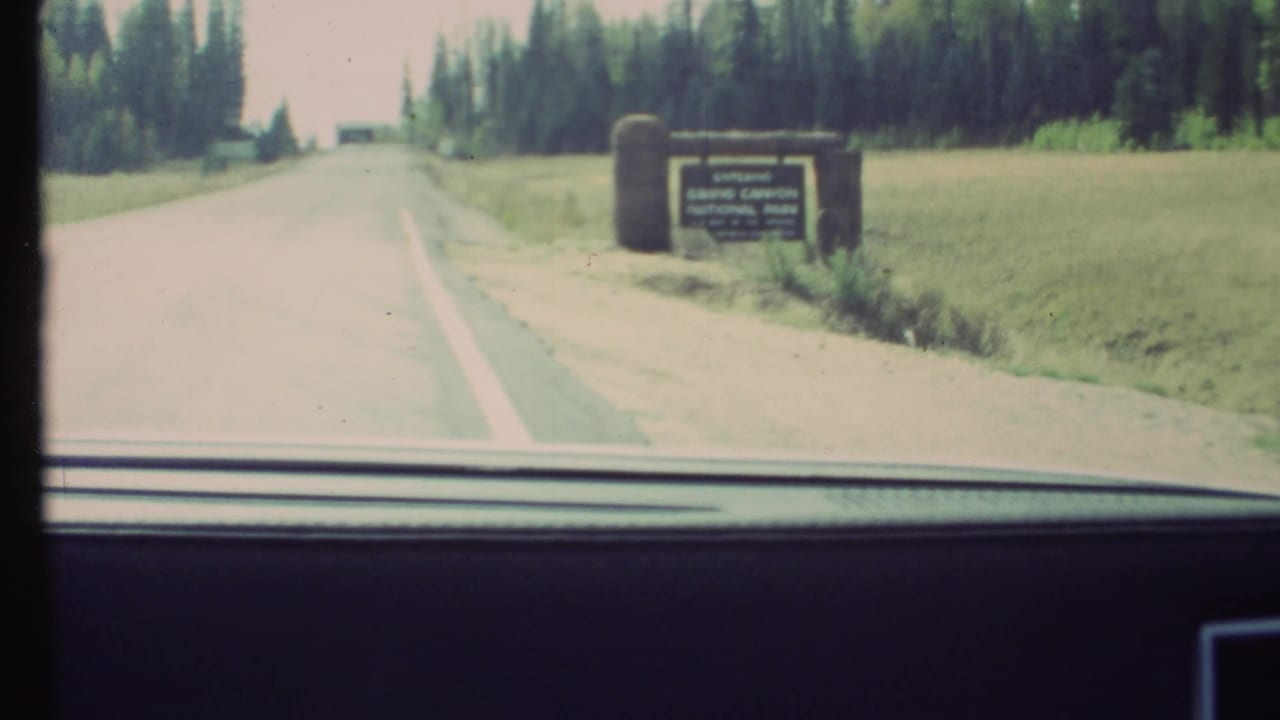 1972 8mm windshield view approaching the Grand Canyon National Park entrance sign on a two-lane road in Arizona.