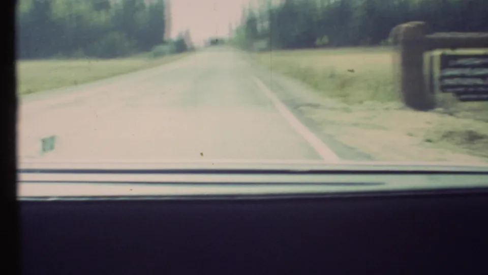 Motion-blurred 1972 8mm view passing the Grand Canyon entrance sign from inside a moving car.