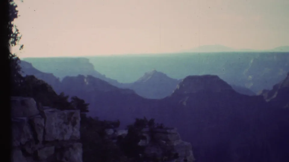 Grand Canyon landscape in soft 1972 8mm color, with dark foreground rocks and hazy layered formations.
