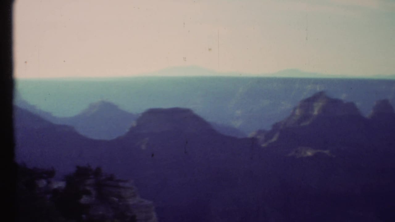 Shadowed canyon ridges beneath a pale sky with film-frame borders visible.