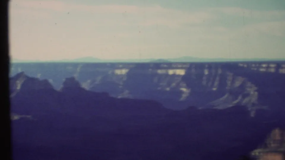 Vintage 8mm view of the Grand Canyon with banded canyon walls, distant mesas, and dark foreground rock forms.