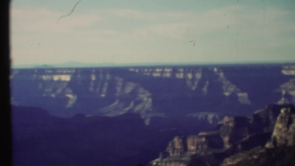 Grand Canyon landscape from a high vantage point, with cliffs, plateau edges, haze, and visible 8mm frame artifacts.