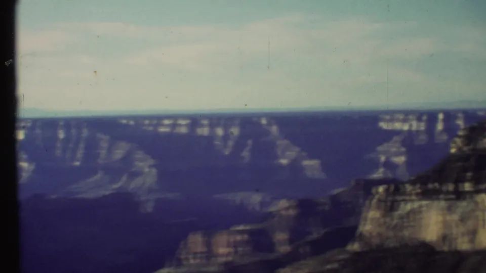 1972 8mm Grand Canyon view from a rim overlook, showing distant layered cliffs and a sunlit foreground formation.