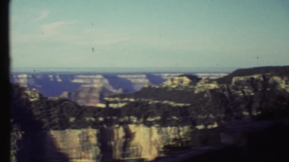 1972 8mm Grand Canyon panorama with dark foreground ridges, layered cliffs, and distant mesas beneath a pale sky.