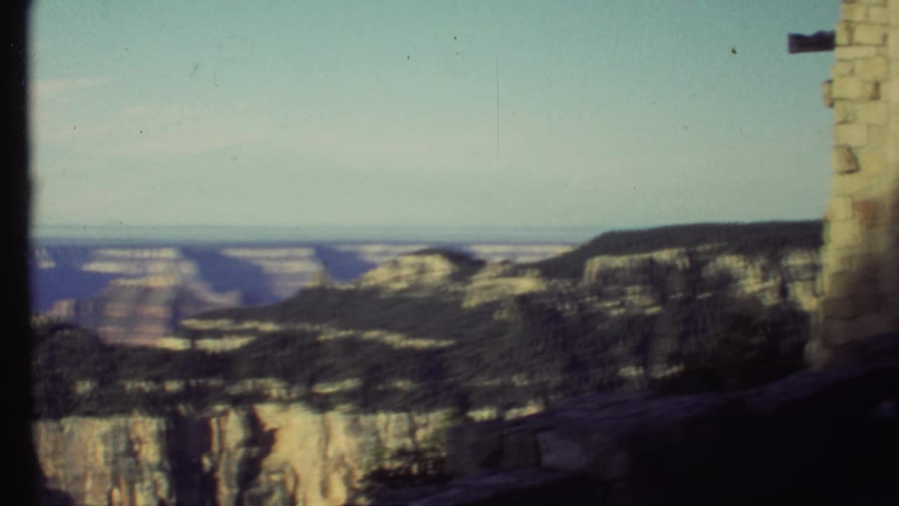 Grand Canyon cliffs and valley seen from a stone overlook under a pale sky.