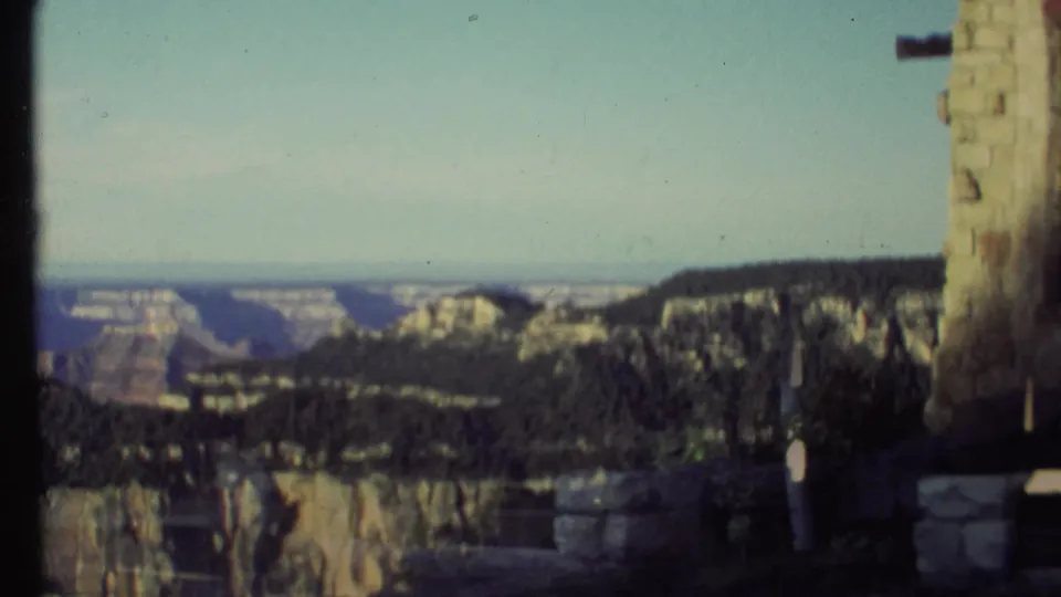 Grand Canyon, Arizona view from a tourist overlook, with canyon ridges, pale sky, stonework, and a dark frame edge from the camera or structure.
