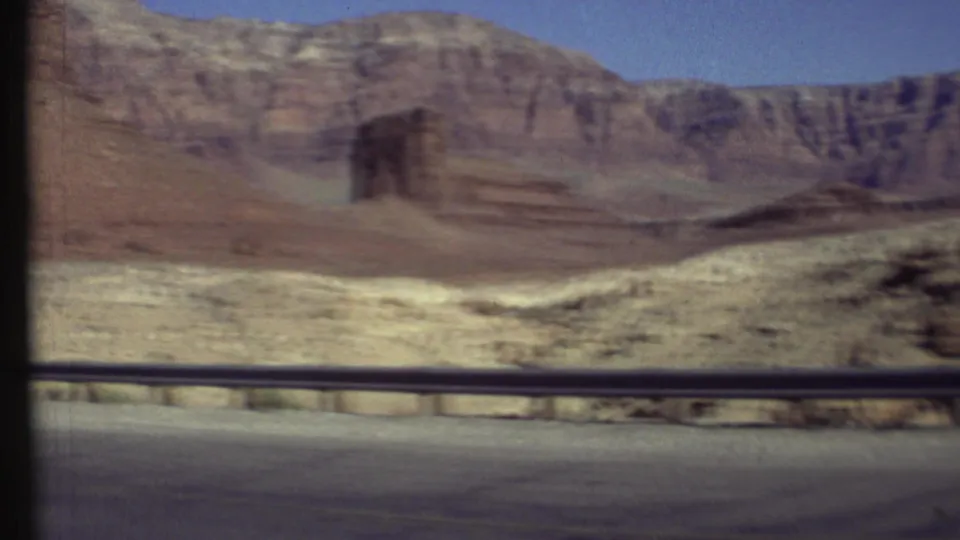 Motion-blurred 8mm view near the Grand Canyon with a guardrail in front of layered cliffs and pale desert slopes.