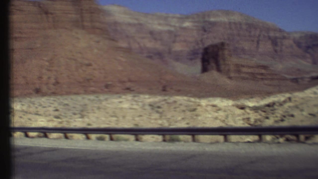 Red rock cliffs beyond a roadside guardrail and paved road edge.