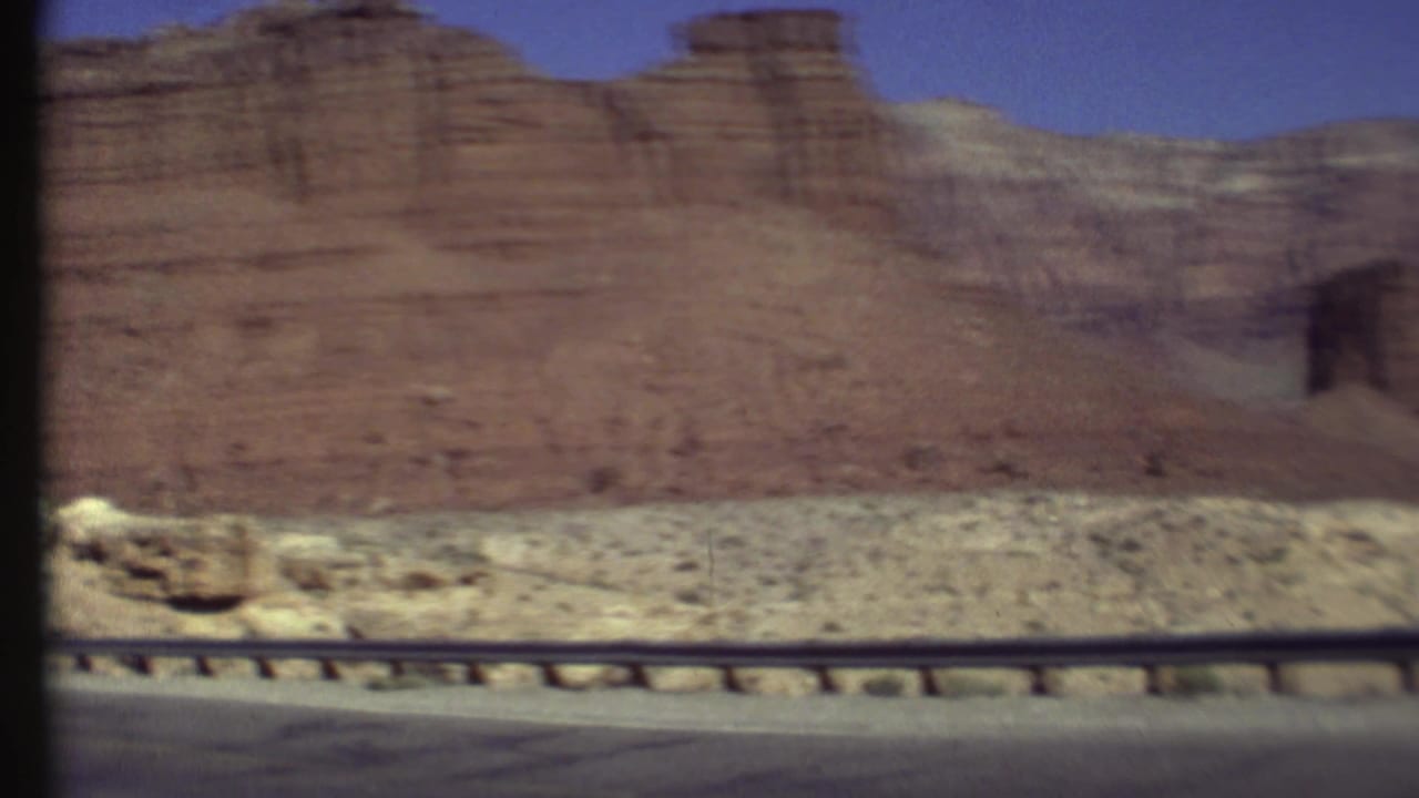Moving 8mm roadside view of a red cliff wall and arid foreground in the Grand Canyon, Arizona area.
