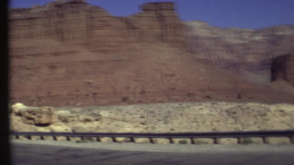 Moving 8mm roadside view of a red cliff wall and arid foreground in the Grand Canyon, Arizona area.