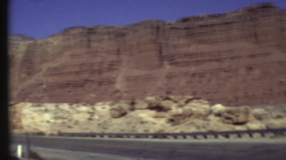 Motion-blurred 8mm view of red rock cliffs, pale desert terrain, and a highway guardrail in the Grand Canyon area.