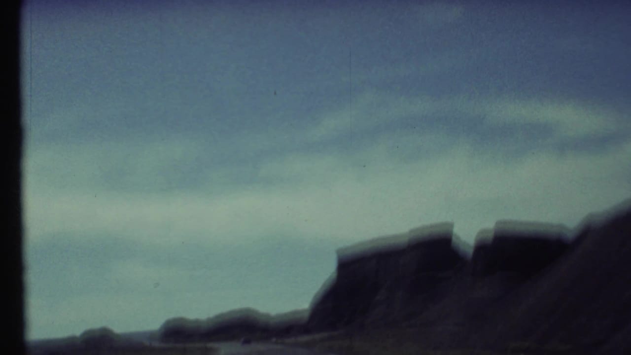 Blurred desert rock silhouettes beneath a blue sky with dark 8mm frame edges.