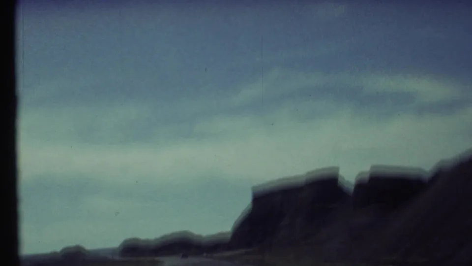 Soft 1972 8mm view near Grand Canyon, Arizona, showing dark desert formations under a blue sky from a moving vehicle.