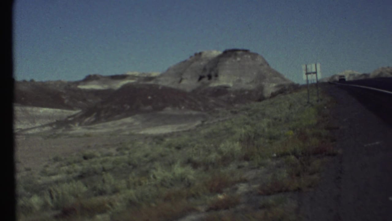 Passenger-side 8mm view of a paved desert road and layered arid hills near Grand Canyon, Arizona, in 1972.