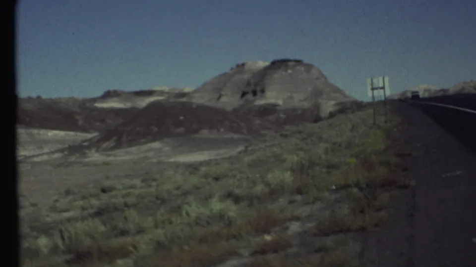 Passenger-side 8mm view of a paved desert road and layered arid hills near Grand Canyon, Arizona, in 1972.