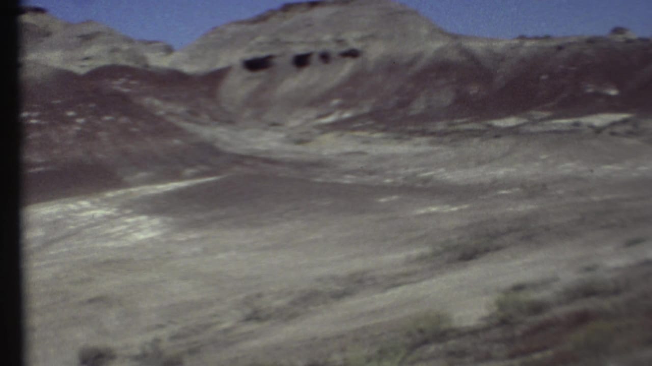 Rocky desert slope with dark eroded bands and dry foreground terrain.