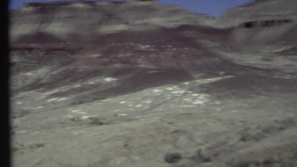 Motion-blurred 8mm frame of Grand Canyon-area desert hills, with layered rock ridges and dry pale terrain.
