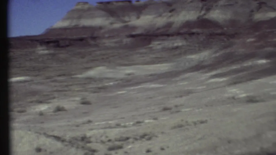 1972 8mm home-movie view near Grand Canyon, Arizona, showing a rocky ridge, sparse scrub, and dry desert ground.