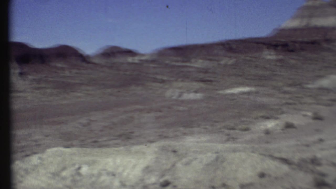 1972 Arizona home-movie frame showing open desert terrain, low ridges, scattered brush, and a pale foreground bank.