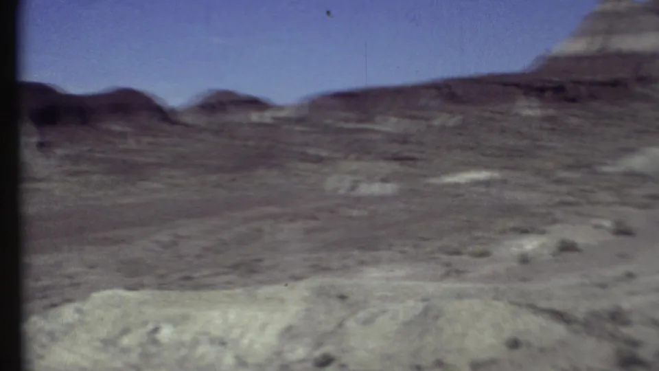 1972 Arizona home-movie frame showing open desert terrain, low ridges, scattered brush, and a pale foreground bank.