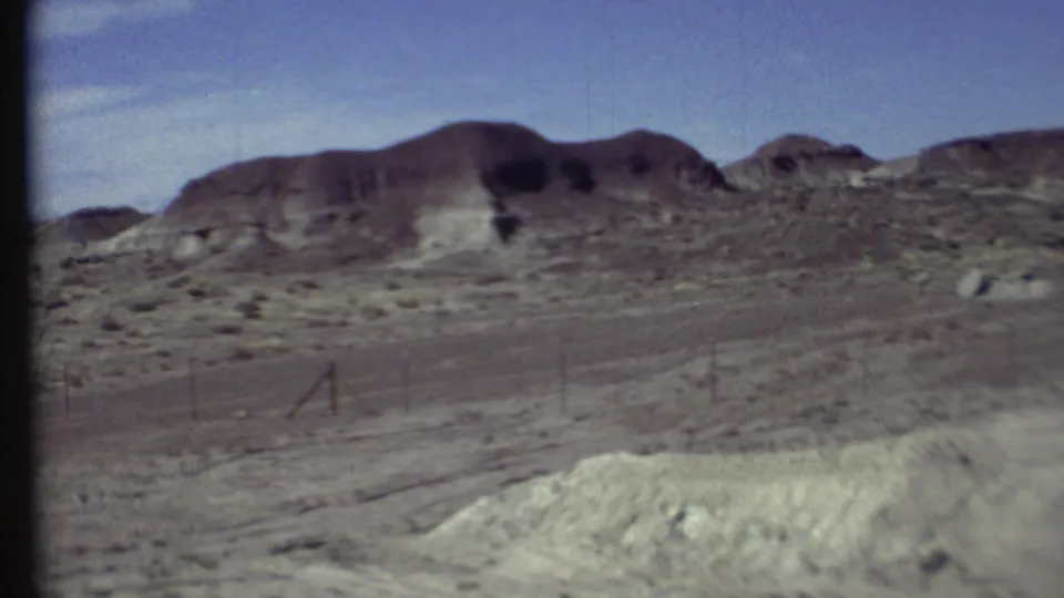 Grand Canyon region landscape in 1972 with a wire fence, dry roadside ground, scrub, and rounded grey-brown hills.