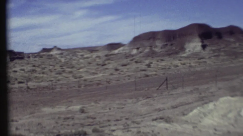 1972 8mm view of fenced scrubland and a broad rounded hill in the Grand Canyon region under a lightly clouded sky.