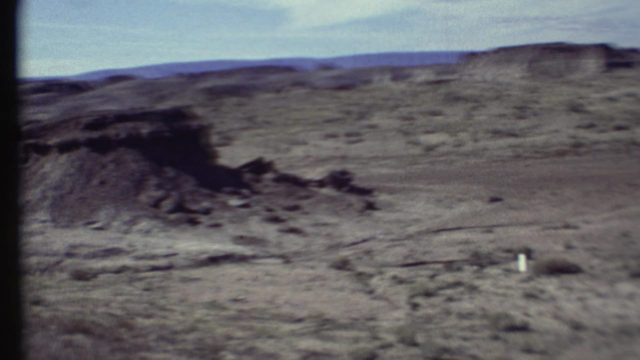 Barren rocky desert terrain with low ridges and sparse scrub under a pale sky.