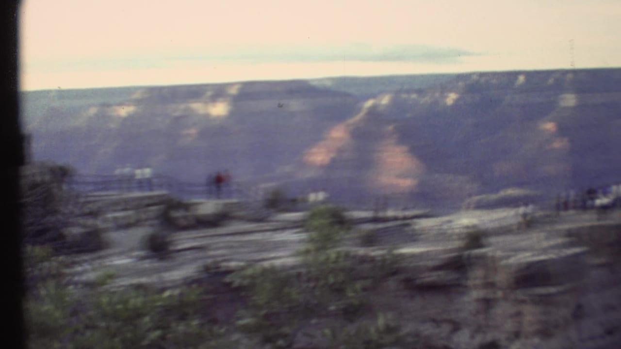 Soft 8mm frame from a Grand Canyon pan, showing visitors near the overlook and broad canyon walls beyond.