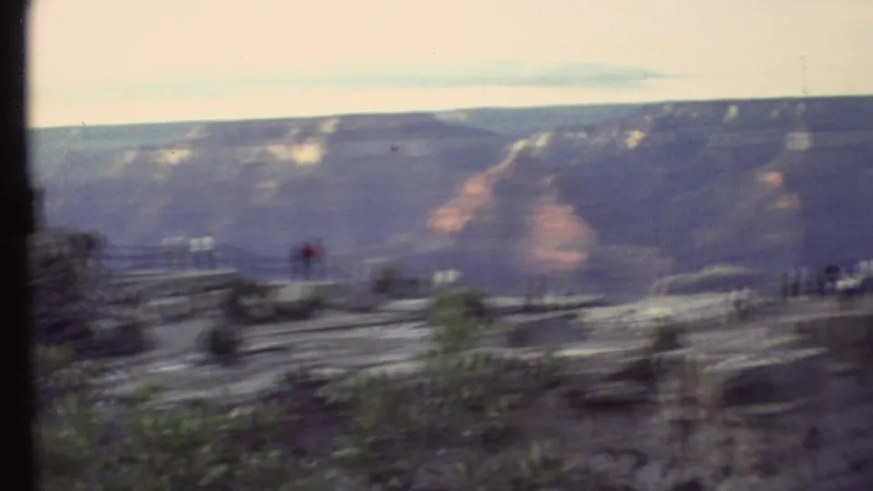 Soft 8mm frame from a Grand Canyon pan, showing visitors near the overlook and broad canyon walls beyond.
