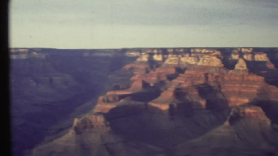 Wide 1972 8mm view of Grand Canyon rock formations, with red-orange cliffs and shadowed ravines.