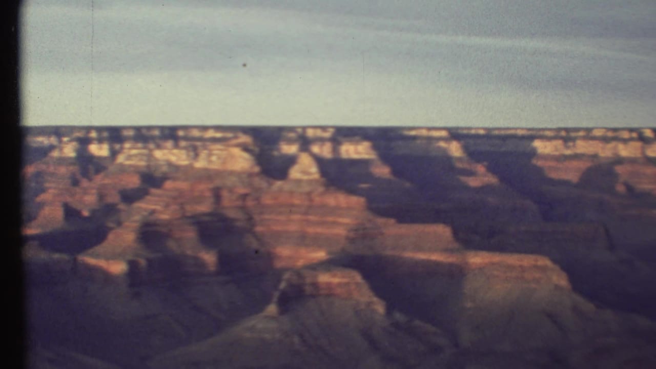1972 Grand Canyon frame with warm red cliffs, distant rim detail, deep canyon shadows, and visible 8mm film softness.