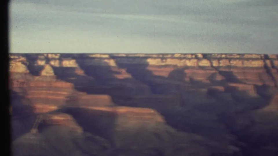 1972 8mm frame showing the Grand Canyon wall during a pan, with layered rock, motion blur, and subdued warm color.