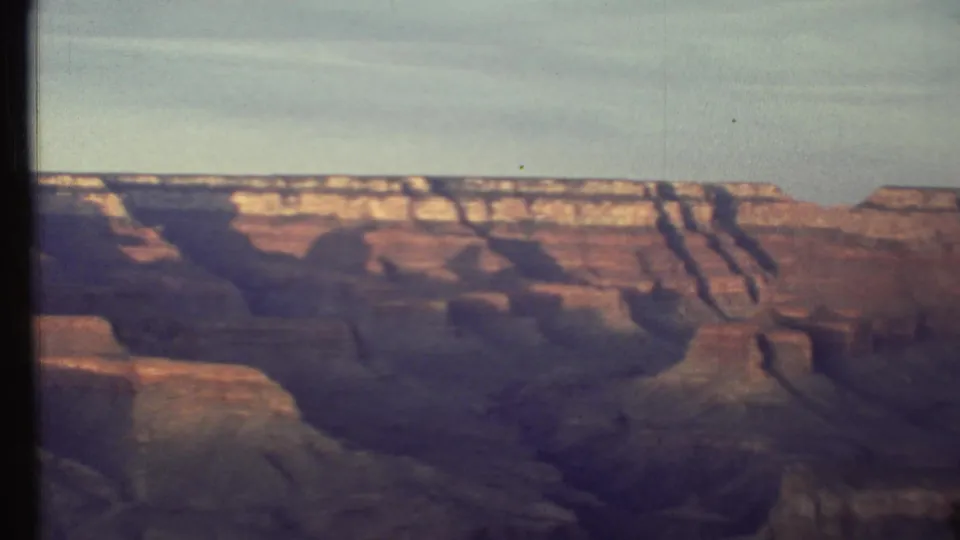 1972 Grand Canyon home-movie frame with distant rim, red and tan rock shelves, broad shadows, and contact-sheet edge marks.