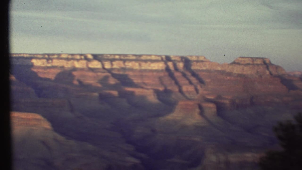 Grand Canyon cliffs and layered rock under a pale sky with film frame edges visible.