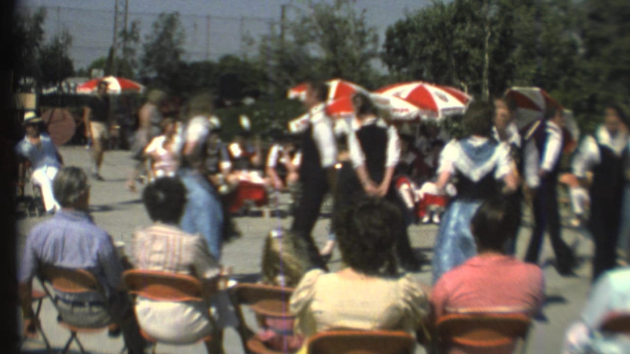 1972 Grand Canyon 8mm frame showing seated spectators watching costumed folk dancers in a sunny outdoor area.