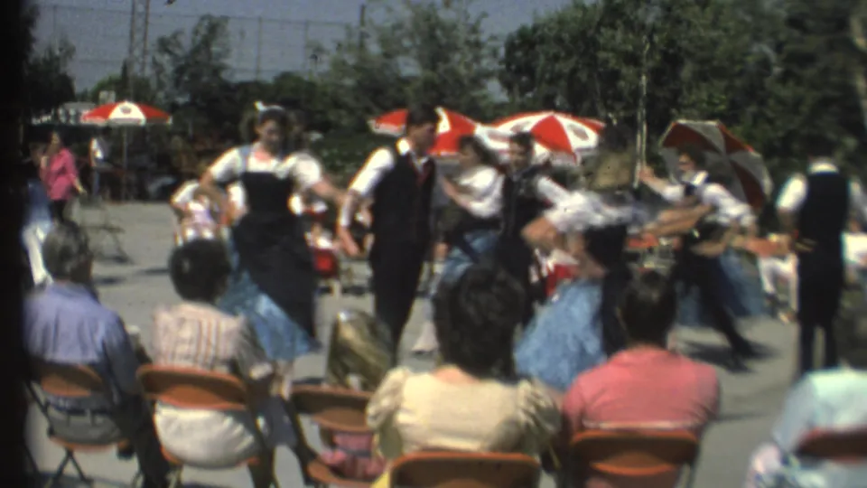 1972 8mm Grand Canyon frame showing a folk dance performance with motion blur, spectators, umbrellas, and trees behind.