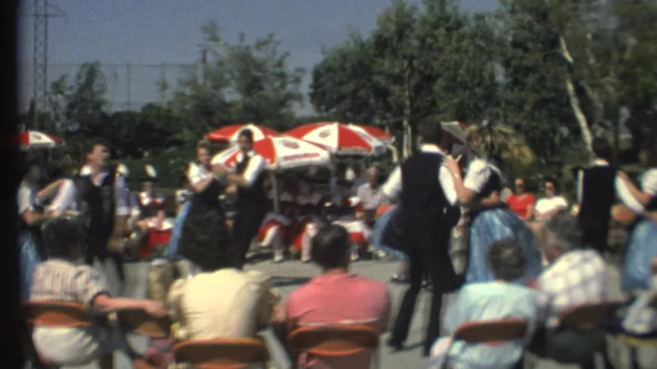 1972 8mm frame of a folk-dance couple passing close to the camera during an outdoor performance before seated viewers.