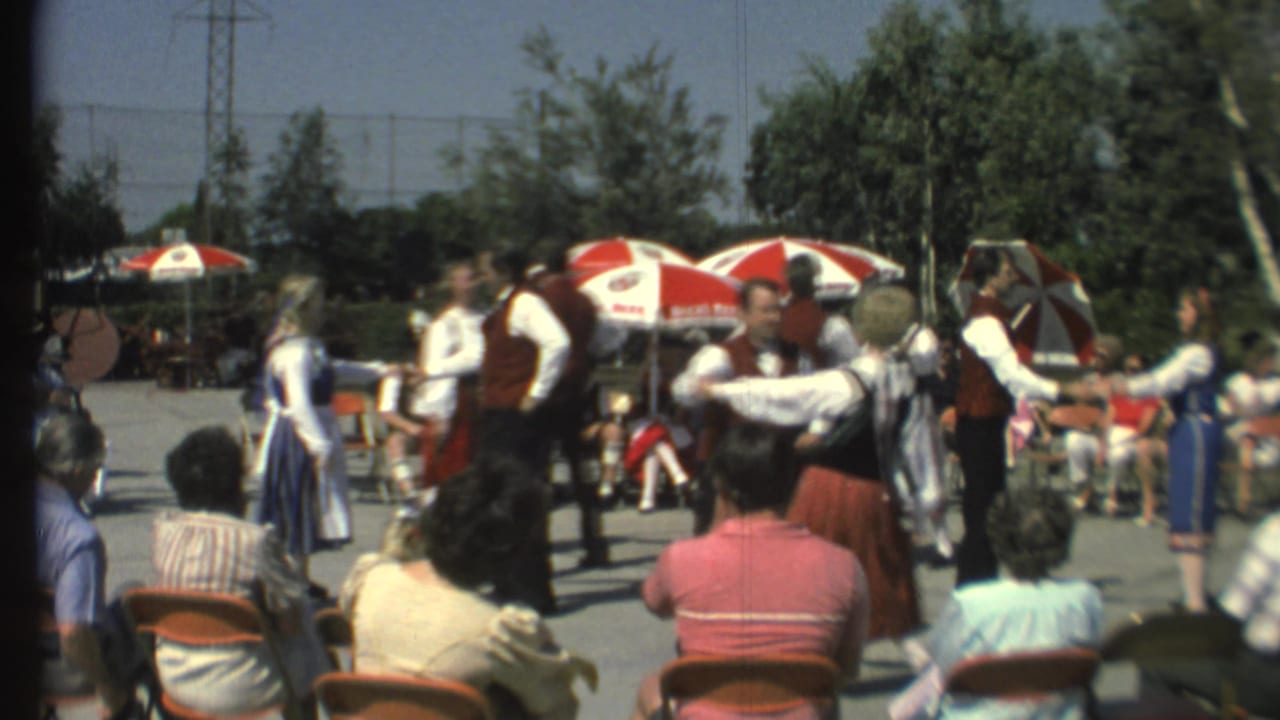 Folk dancers perform in front of seated spectators at an outdoor festival.