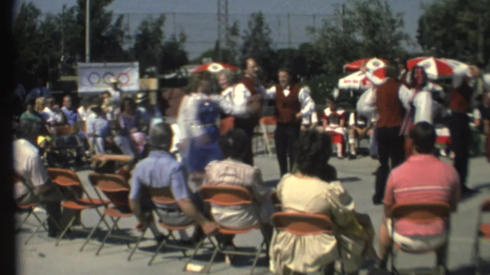 Grand Canyon 1972 home-movie frame showing seated spectators, folk dancers, umbrellas, and a small Olympic-ring banner.