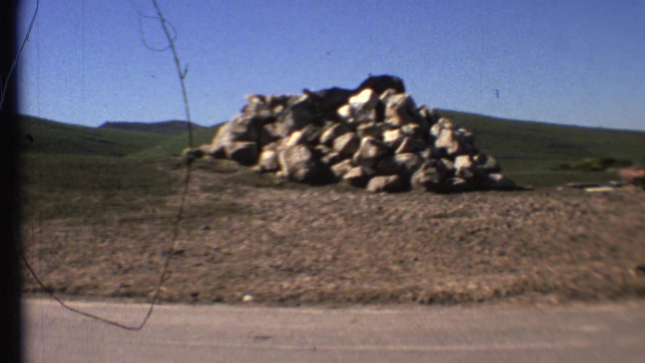 Rock pile beside a paved road with rolling green hills and blue sky beyond.