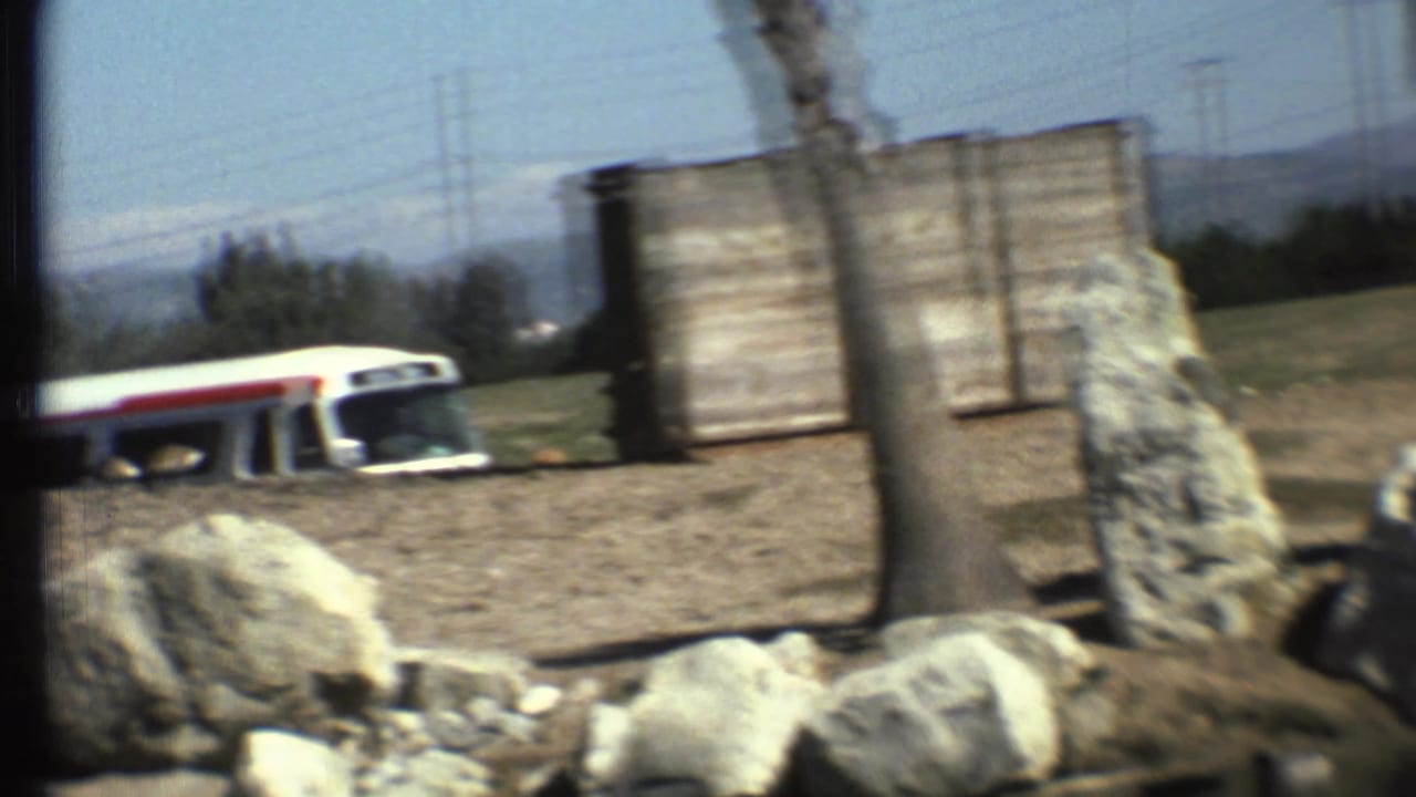 White bus with a red stripe partly visible beyond rocks and a wooden structure.