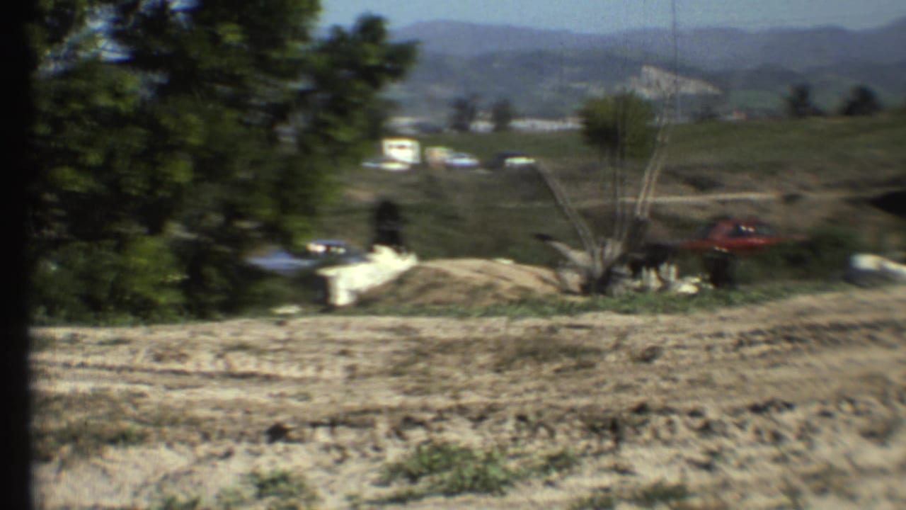 1972 Grand Canyon, Arizona home-movie frame showing monkeys near pale rocks and brush, with a red car and distant hills behind them.