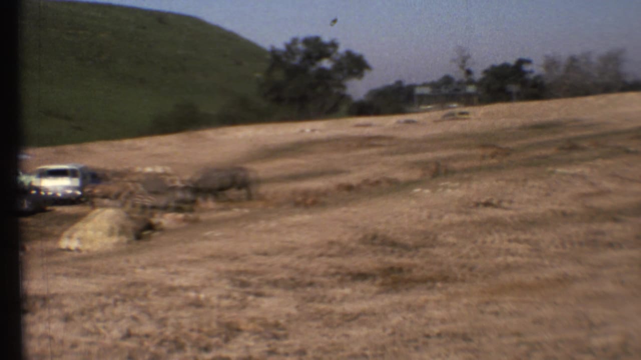 Dirt road and dry hillside with a white vehicle at the left edge.