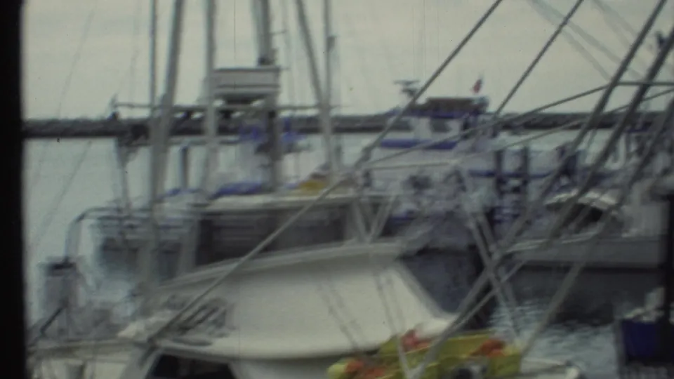 1972 8mm frame looking across moored marina boats with masts, rigging, dock structures, and muted home-movie color.