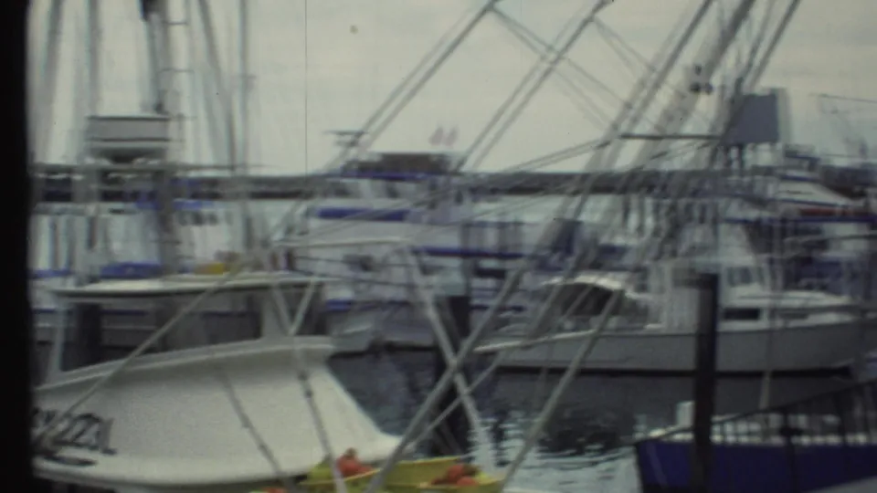 1970s 8mm home-movie view of multiple boats moored in a crowded harbor, with metal frames crossing the foreground.