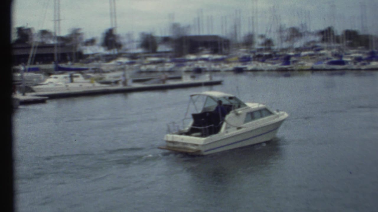 1972 8mm frame showing the motorboat farther across the marina, leaving a faint wake below rows of moored sailboats.