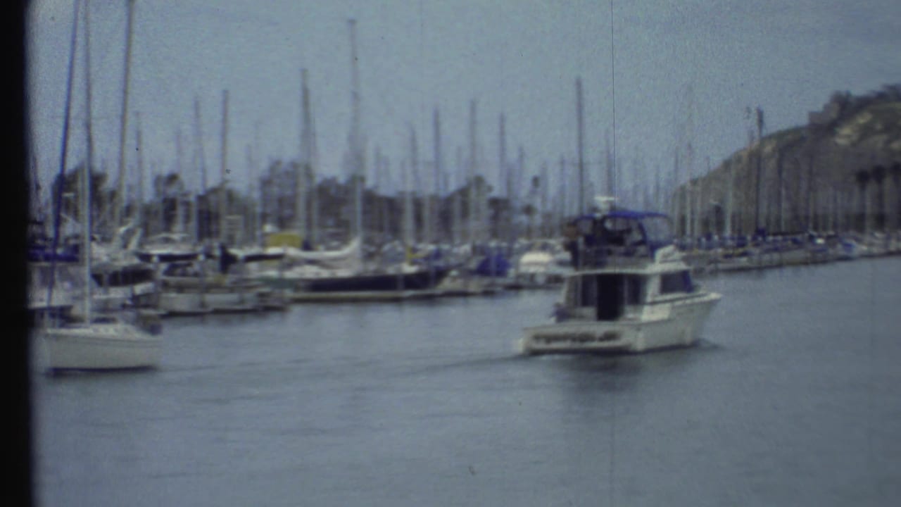 Motorboat with a blue canopy moving through a marina beside many docked sailboats.